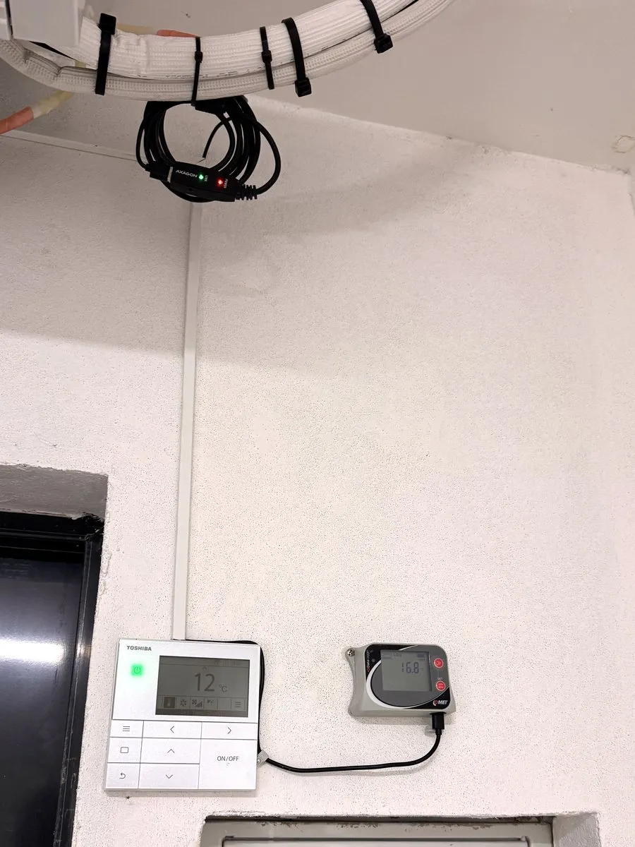 Datalogger Comet vedle ovladače klimatizace na stěně skladu